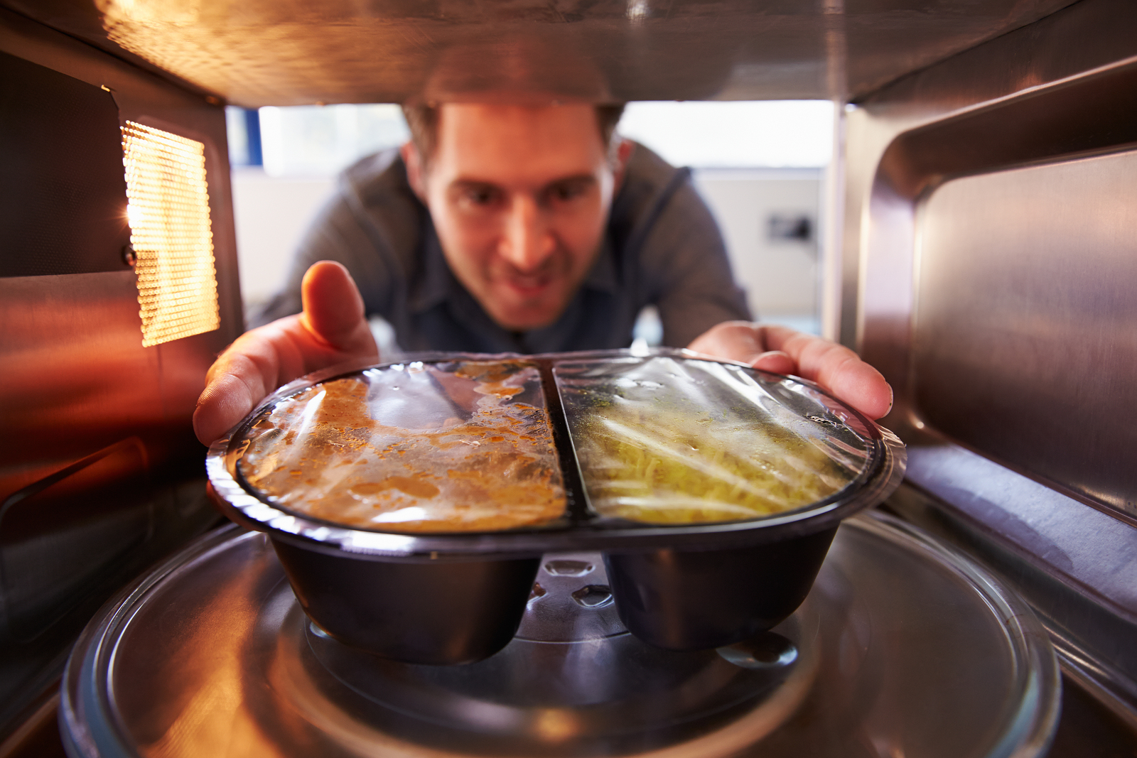 Man Putting TV Dinner Into Microwave Oven To Cook